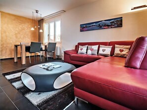 A modern living room with a red leather sofa, a round coffee table, and a dining area with chairs and a table. - Brüggli A14 Appartement/Fewo, Bad, WC, 4-Bettwohnung by Interhome (Arosa)