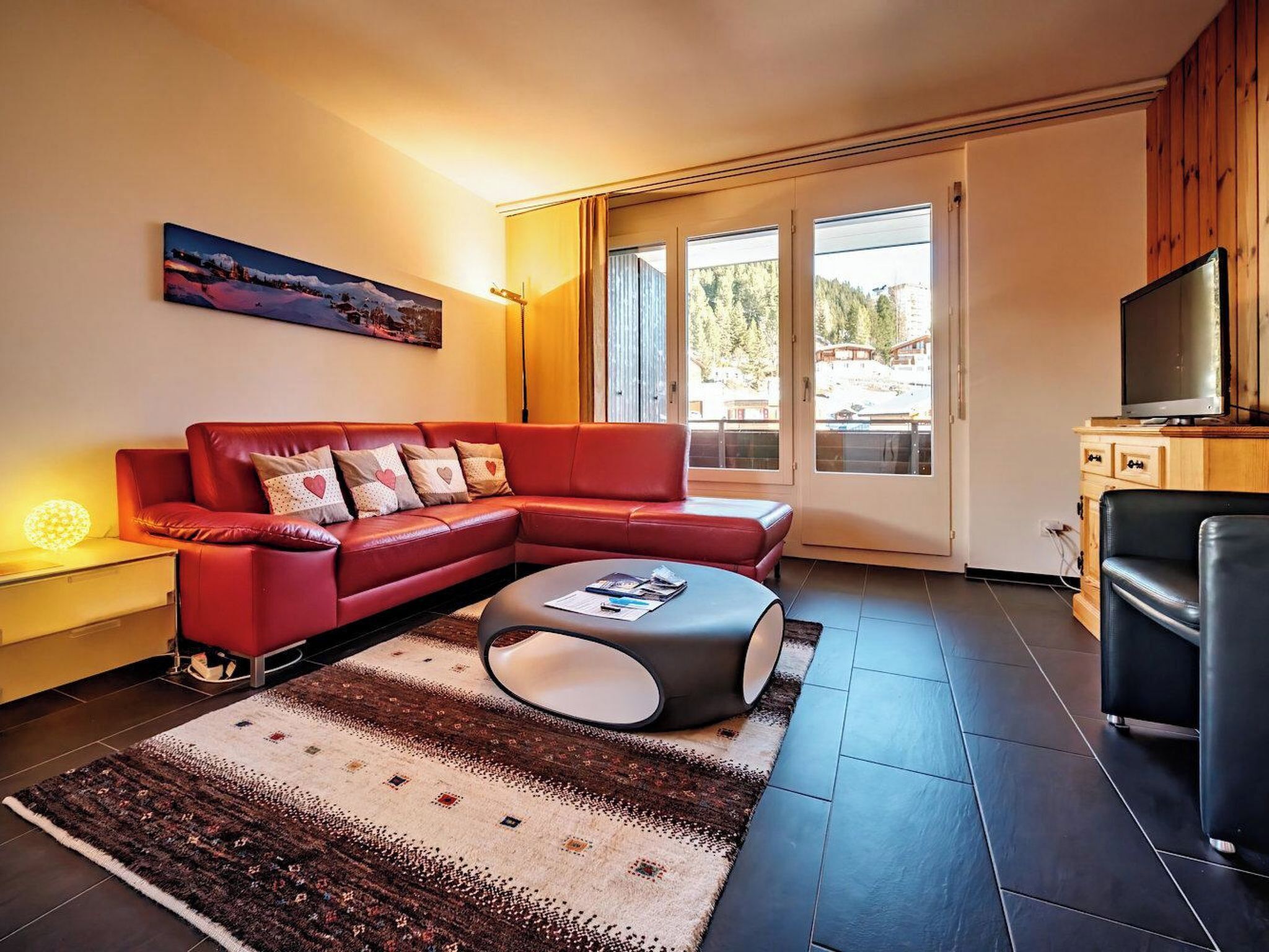 Ein modernes Wohnzimmer mit einem roten Sofa, einem Couchtisch und einem Fernseher auf einer Holzkommode.