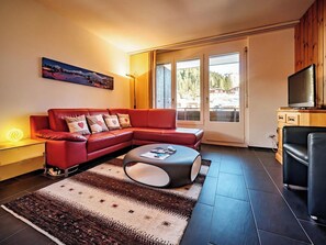 A modern living room with a red sofa, a coffee table, and a television on a wooden cabinet. - Brüggli A14 Appartement/Fewo, Bad, WC, 4-Bettwohnung by Interhome (Arosa)