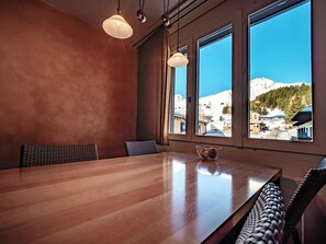 Et træbord med stole, store vinduer med udsigt til et snækkedækket bjerg, og hængende lamper.