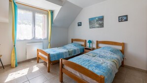 Een slaapkamer met twee houten bedden, een raam met gordijnen, een radiator en een klein tafeltje met een lamp.