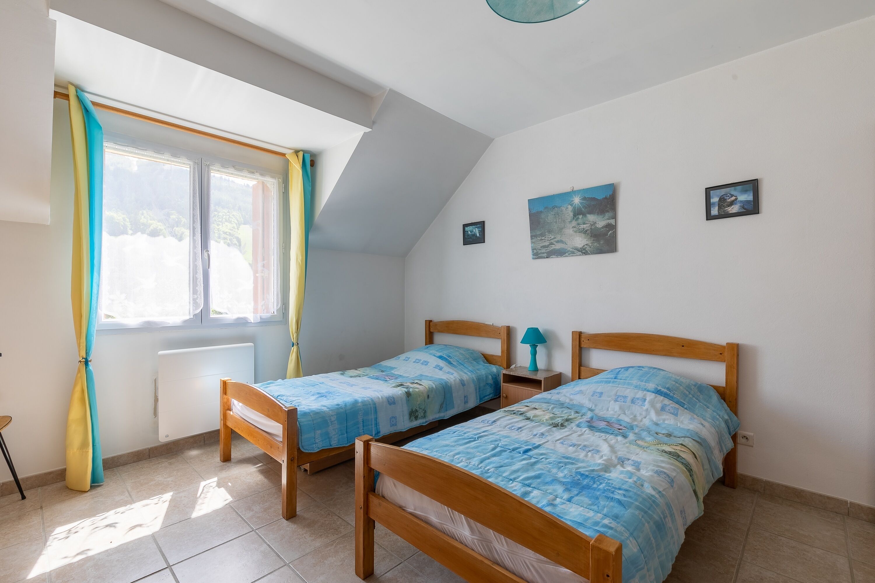 A bedroom with two wooden beds, a window with curtains, a radiator, and a small table with a lamp. - L'Oustaou des Adrets - Proche station de ski (Le Lauzet-Ubaye)