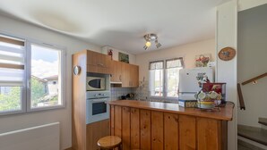 Een keuken met houten kastjes, een centraal eiland met krukken, een magnetron, een oven en een koelkast.