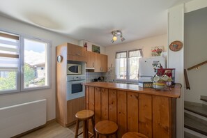 A kitchen with wooden cabinets, a central island with stools, a microwave, an oven, and a refrigerator. - L'Oustaou des Adrets - Proche station de ski (Le Lauzet-Ubaye)