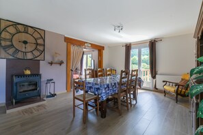 A dining area with a wooden table, chairs, a large wall clock, and a fireplace. - L'Oustaou des Adrets - Proche station de ski (Le Lauzet-Ubaye)