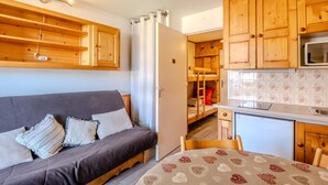 Una habitación compacta con sofá, una mesita, armarios de madera, microondas y refrigerador.
