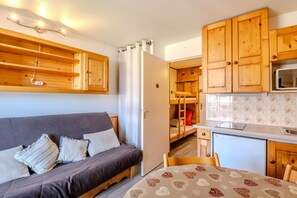 A compact room with a sofa, a small table, wooden cabinets, a microwave, and a refrigerator. - Studio Samoëns - Station de ski accessible à pied (Samoëns)