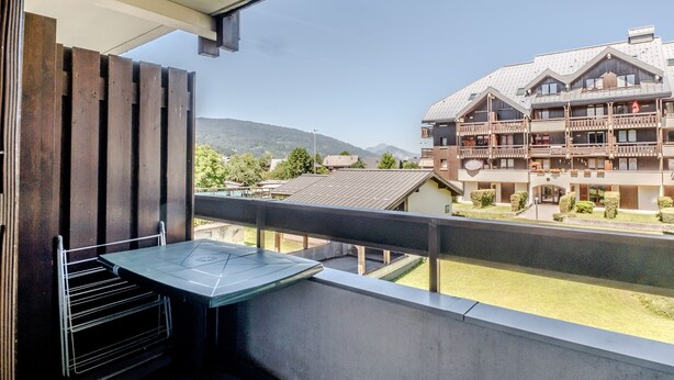Un balcón con una mesa y sillas, con vistas a un edificio que tiene varios balcones y un paisaje montañoso de fondo.