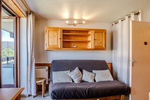 A bedroom with a bed, wooden headboard, bedside table, and a window with curtains. - Studio Samoëns - Station de ski accessible à pied (Samoëns)