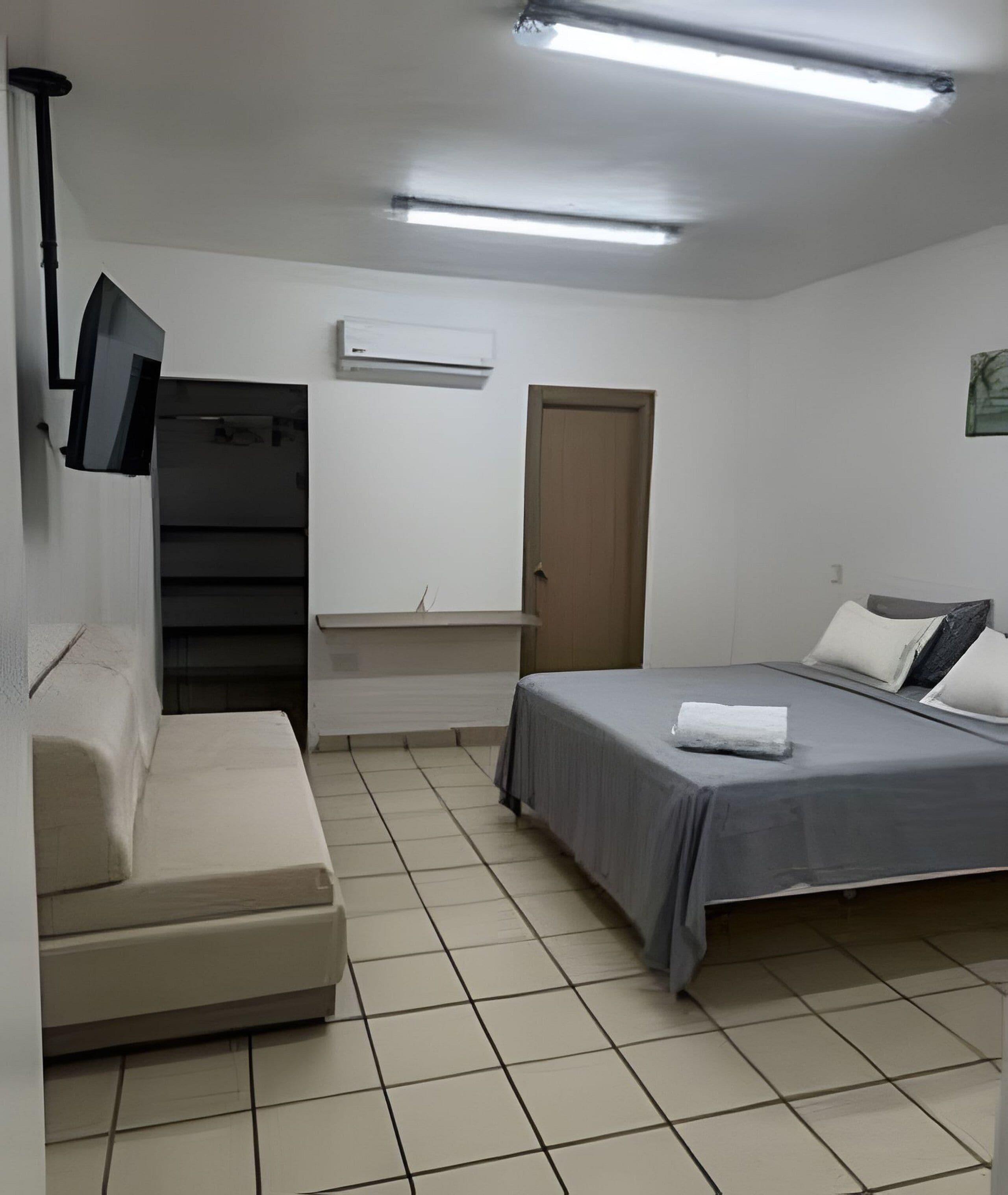 A bedroom with a bed, a sofa, a television, and a door.