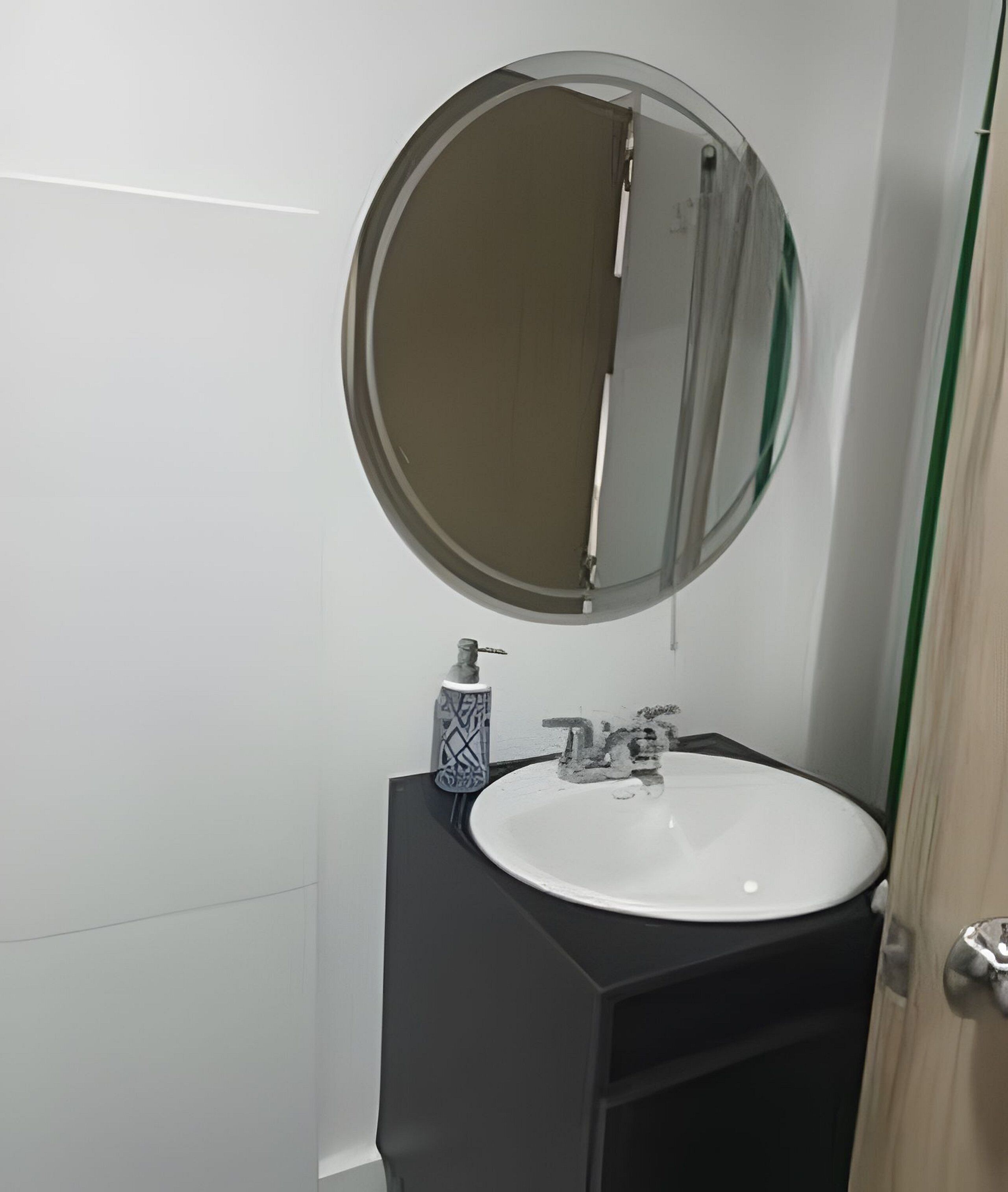 A bathroom with a round mirror, a white sink, and a black cabinet.