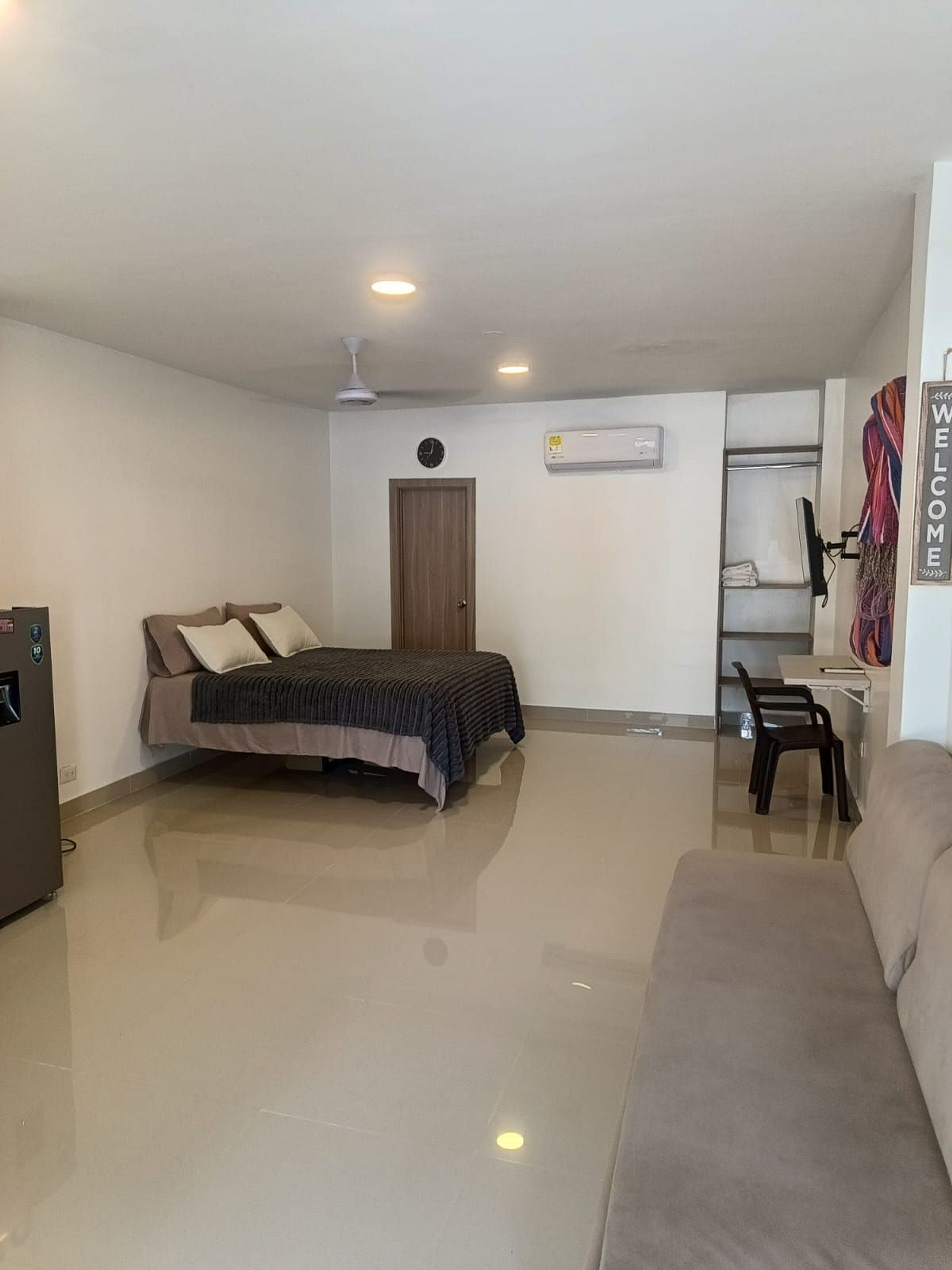 Quarto com cama, escrivaninha, cadeira, guarda-roupa e frigorífico.