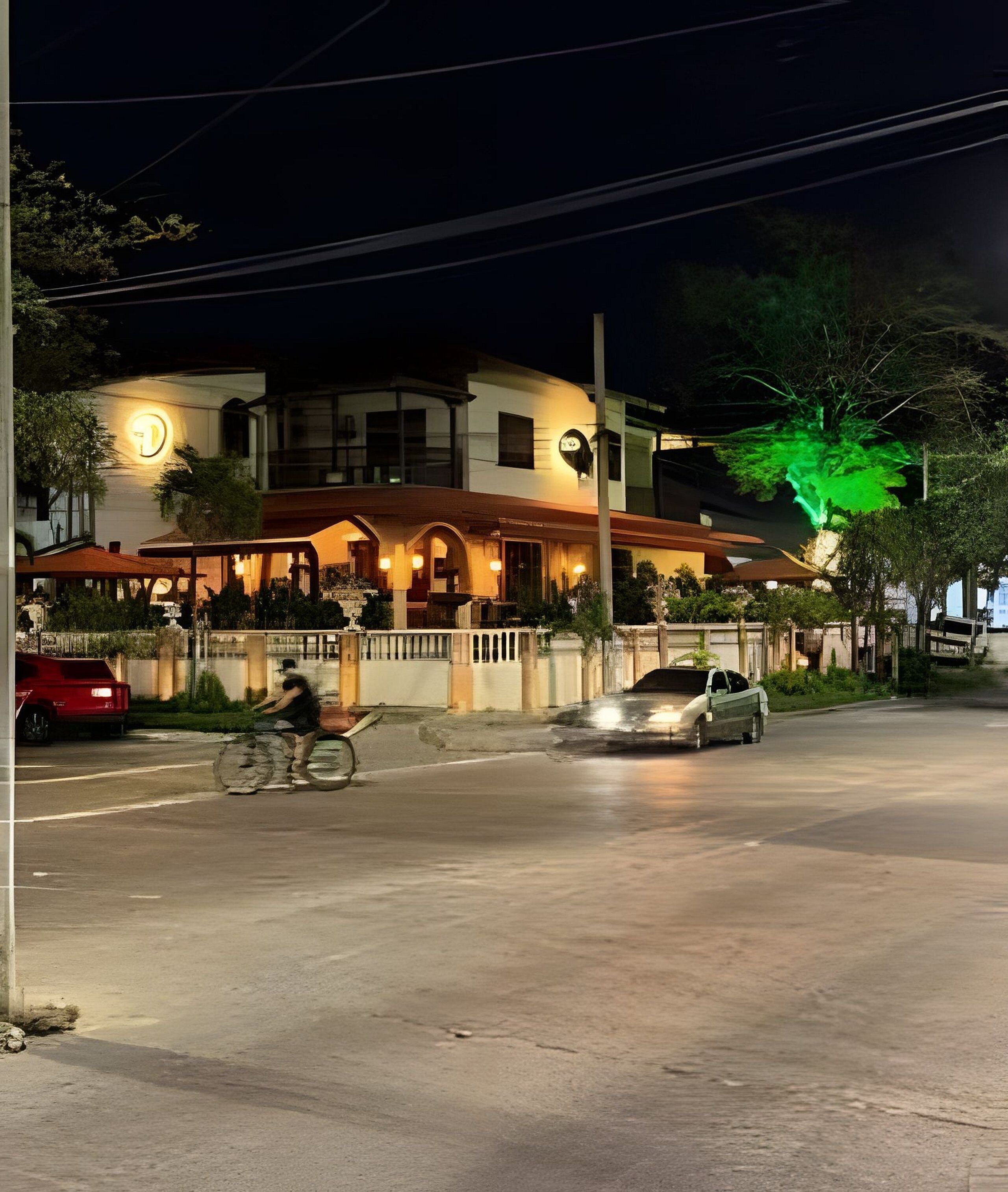 A building with a large illuminated sign, a covered outdoor seating area, and a street with vehicles.