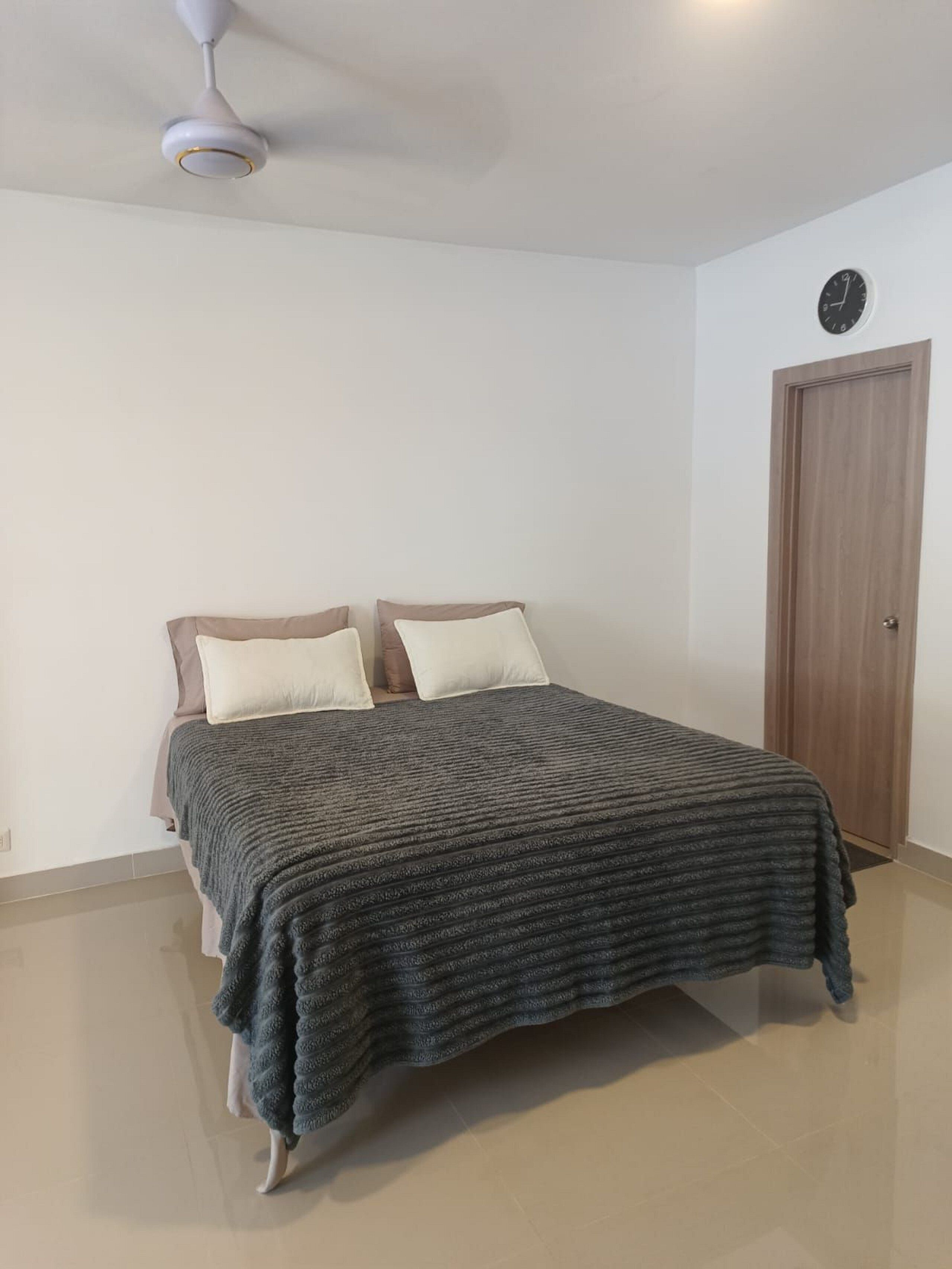 Un dormitorio con cama, almohadas, una puerta de madera y un ventilador de techo.