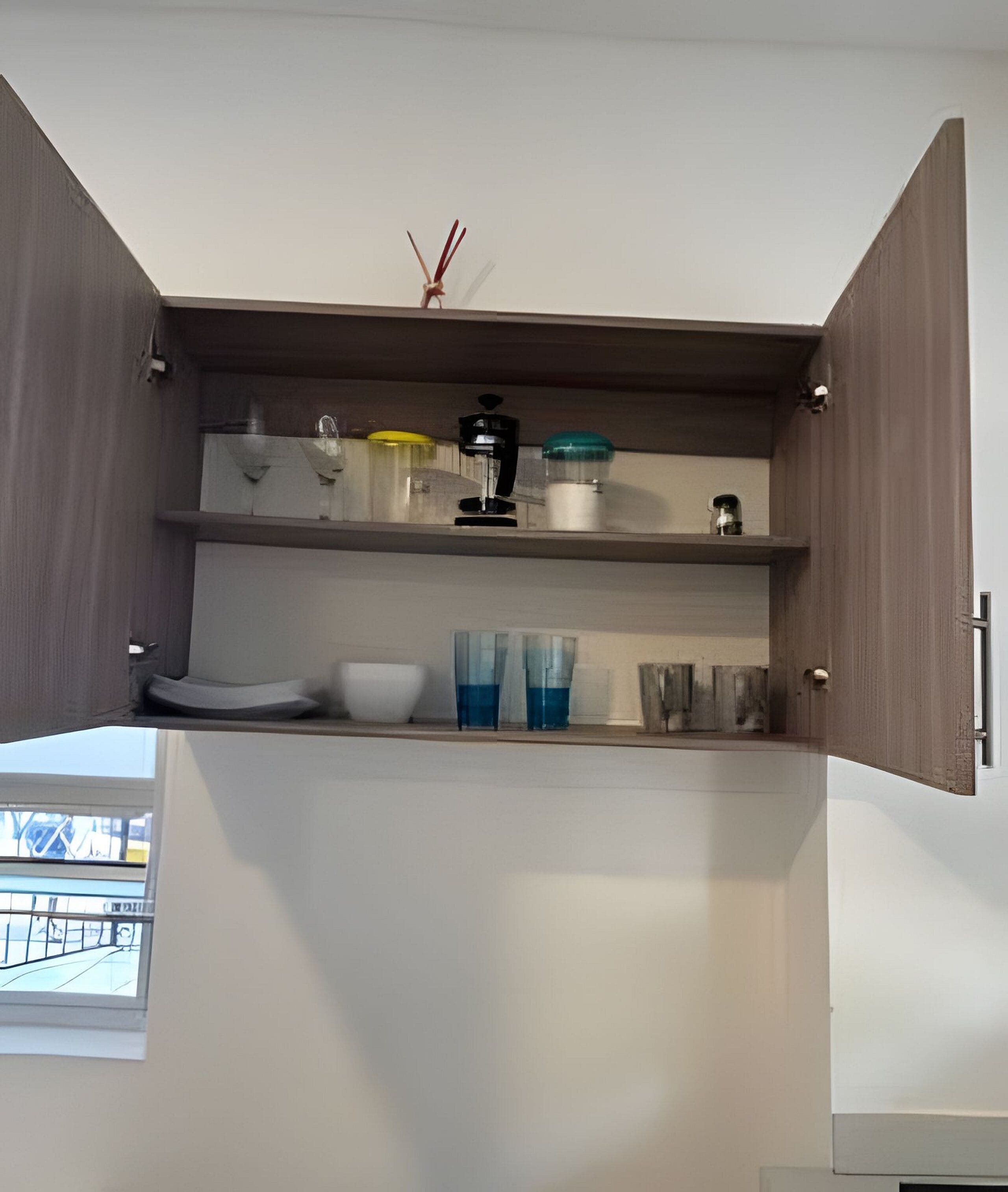 A kitchen with open cabinets, a coffee maker, a bowl, and a glass container.