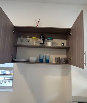 Una cocina con armarios abiertos, una cafetera, un bol y un recipiente de vidrio.