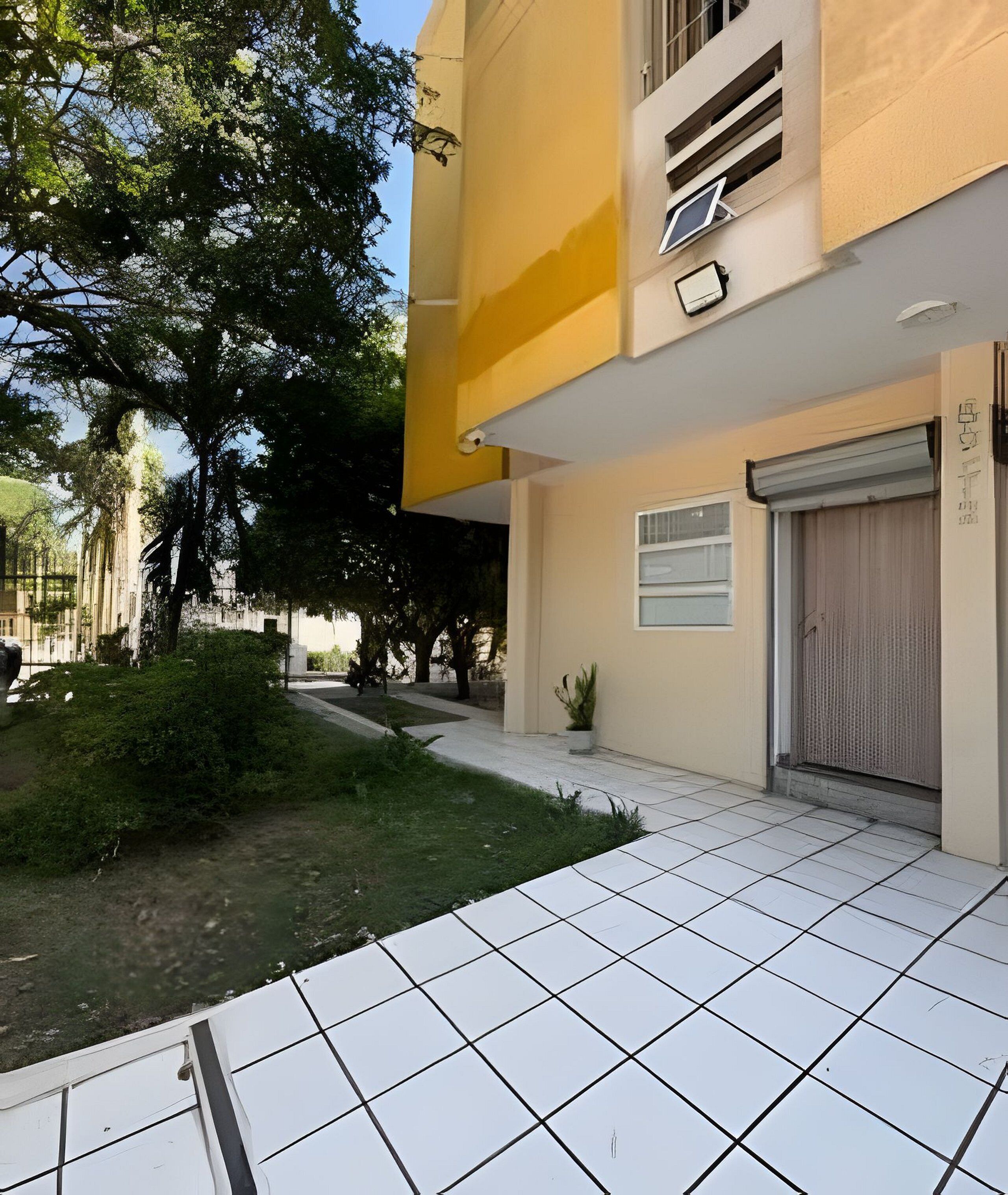 A building with a tiled entrance, a closed garage door, and a small garden area with trees and shrubs.
