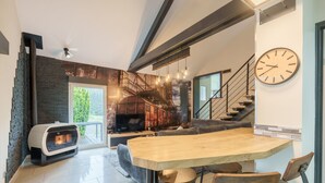 A modern living room with a fireplace, a dining area with a wooden table, and a staircase. - Notre écrin vosgien - Belle maison avec jacuzzi (Plainfaing)