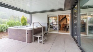 A modern outdoor hot tub area with a glass door leading to a dining area. - Notre écrin vosgien - Belle maison avec jacuzzi (Plainfaing)