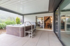 A modern outdoor hot tub area with a glass door leading to a dining area. - Notre écrin vosgien - Belle maison avec jacuzzi (Plainfaing)