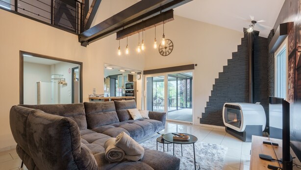 A modern living room with a large sofa, a fireplace, a television, and a staircase. - Notre écrin vosgien - Belle maison avec jacuzzi (Plainfaing)
