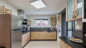 A modern kitchen with a stainless steel refrigerator, wooden cabinets, a black countertop, and a window with a view of trees. - Notre écrin vosgien - Belle maison avec jacuzzi (Plainfaing)