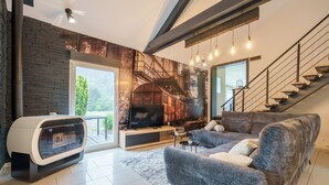 A modern living room with a fireplace, a large sofa, a television, and a staircase. - Notre écrin vosgien - Belle maison avec jacuzzi (Plainfaing)