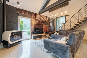 A modern living room with a fireplace, a large sofa, a television, and a staircase. - Notre écrin vosgien - Belle maison avec jacuzzi (Plainfaing)