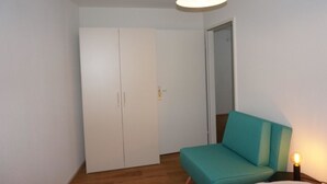 A bedroom with a teal sofa, a wardrobe, and a hanging light fixture. - Paradies 017 Appartement/Fewo,   4-Bettwohnung by Interhome (Arosa)