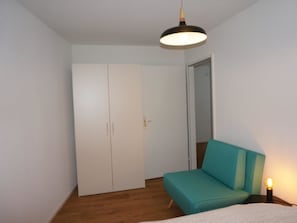 Ein Schlafzimmer mit einem hölzernen Sofa in Türkis, einem Kleiderschrank und einer Pendelleuchte.