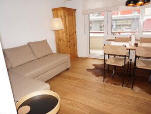 Een kamer met een bank, een eettafel met stoelen, een lamp en een houten kast.