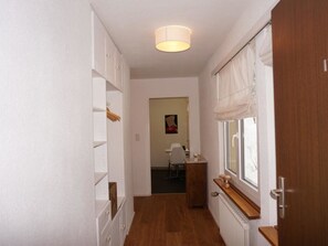 Een gang met witte schapkasthuisjes, een radiator en een raam met gordijn.