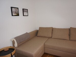 Ein braunes Sofa mit Kissen, ein kleiner runder Tisch mit einem Gegenstand darauf und zwei gerahmte Bilder an der Wand.