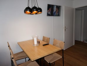 Ein Essbereich mit einem Holztisch, vier Stühlen, einer Fernbedienung und einer Kerze in einem Glas.