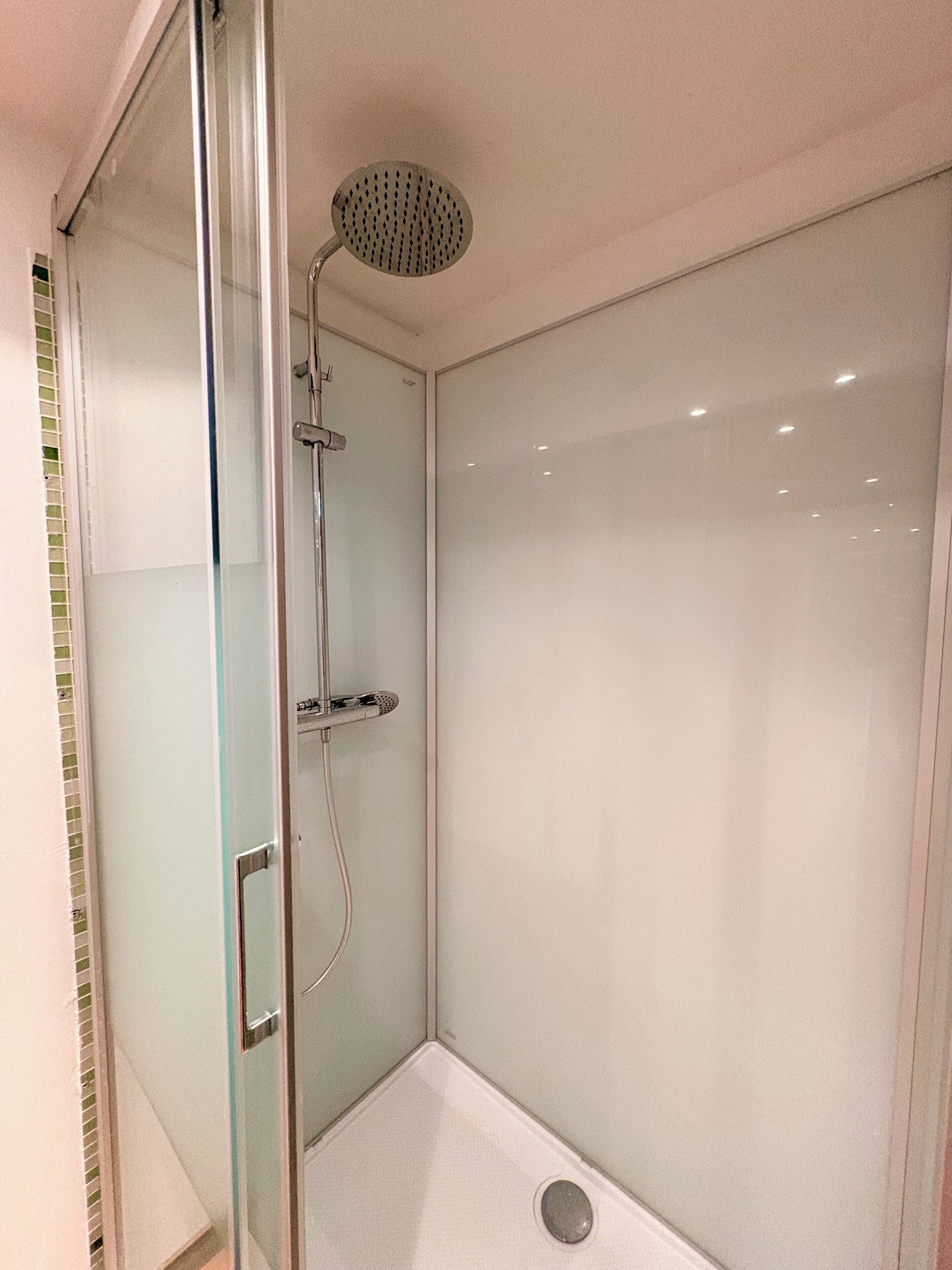 A glass-enclosed shower stall with a handheld showerhead and a wall-mounted faucet.
