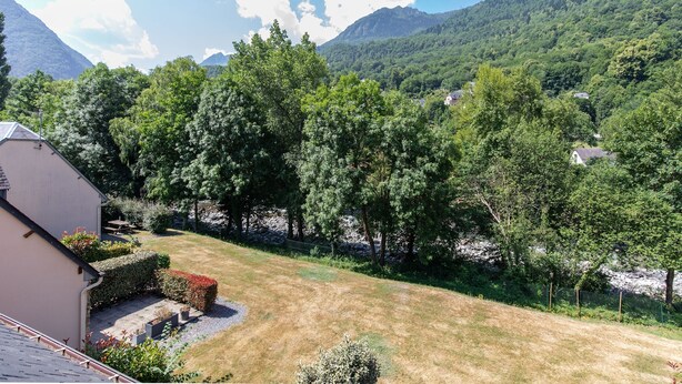 Un quartier résidentiel avec une maison, une pelouse bien entretenue et un paysage montagneux en arrière-plan.