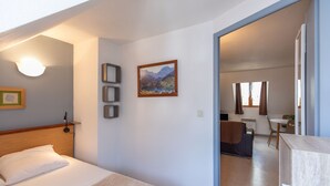 Une chambre d’hôtel comprenant un lit, un bureau, une chaise, un tableau et donnant sur la salle à manger.
