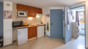Une cuisine compacte équipée d’un four à micro-ondes, d’une cuisinière et d’un lave-vaisselle, avec des meubles en bois et une porte bleue.