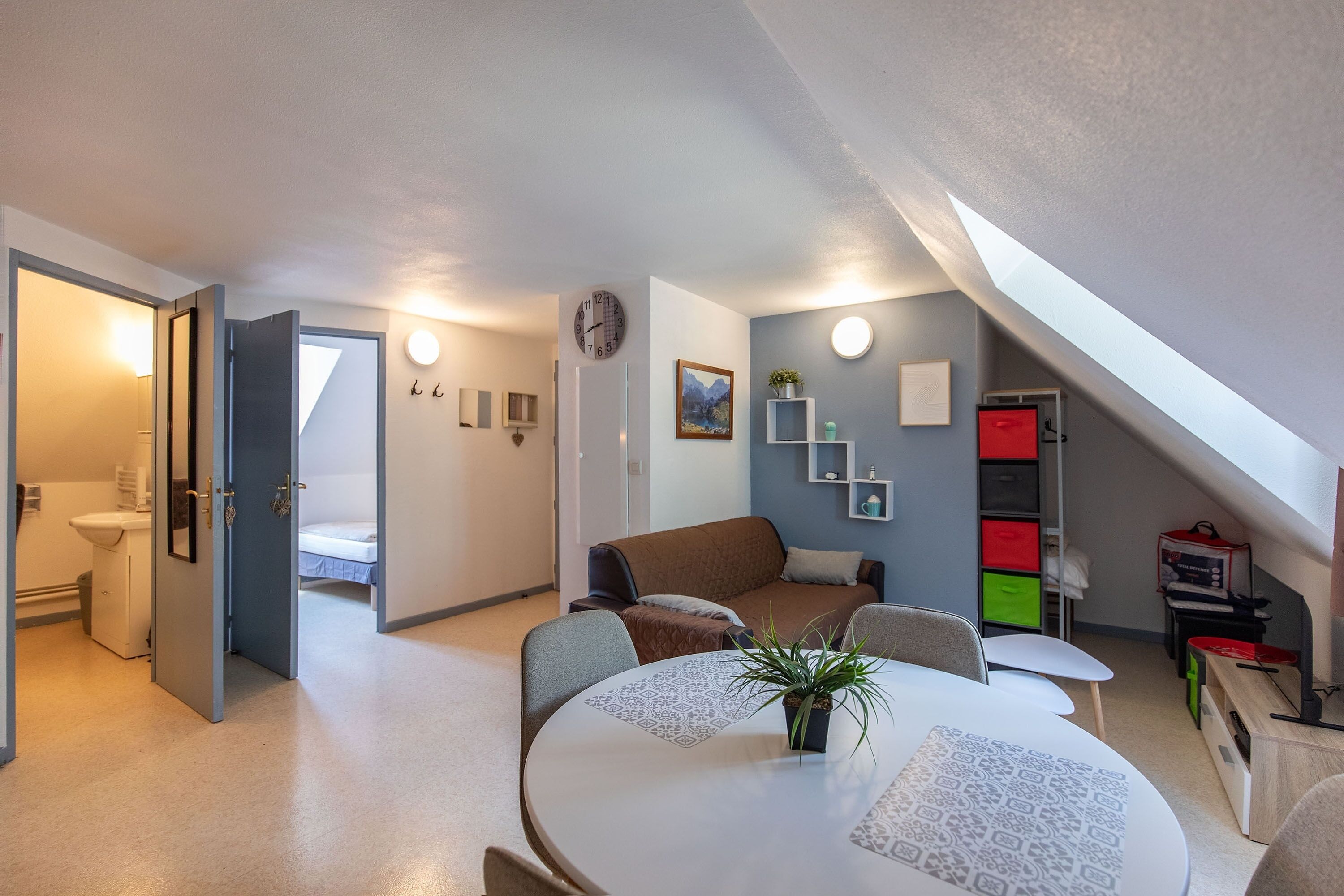 Ein modernes Wohnzimmer mit rundem Tisch, einer Couch, einer Uhr und einer Treppe, die in ein Obergeschoss führt.