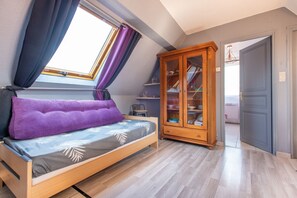 Une chambre à coucher avec un lit, une fenêtre avec des rideaux, une armoire en bois et une porte donnant sur une autre pièce.