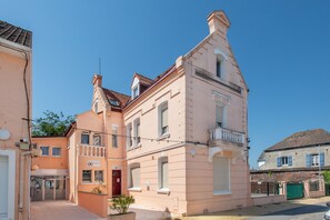 Un bâtiment rose doté d’un balcon, d’une porte rouge et d’un petit jardin.