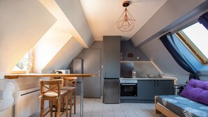 A compact kitchen with a dining area, a bed with a purple pillow, and a skylight. - Chez Cathy - Cocon pour 2 à 15 min de la plage (Etaples-sur-Mer)