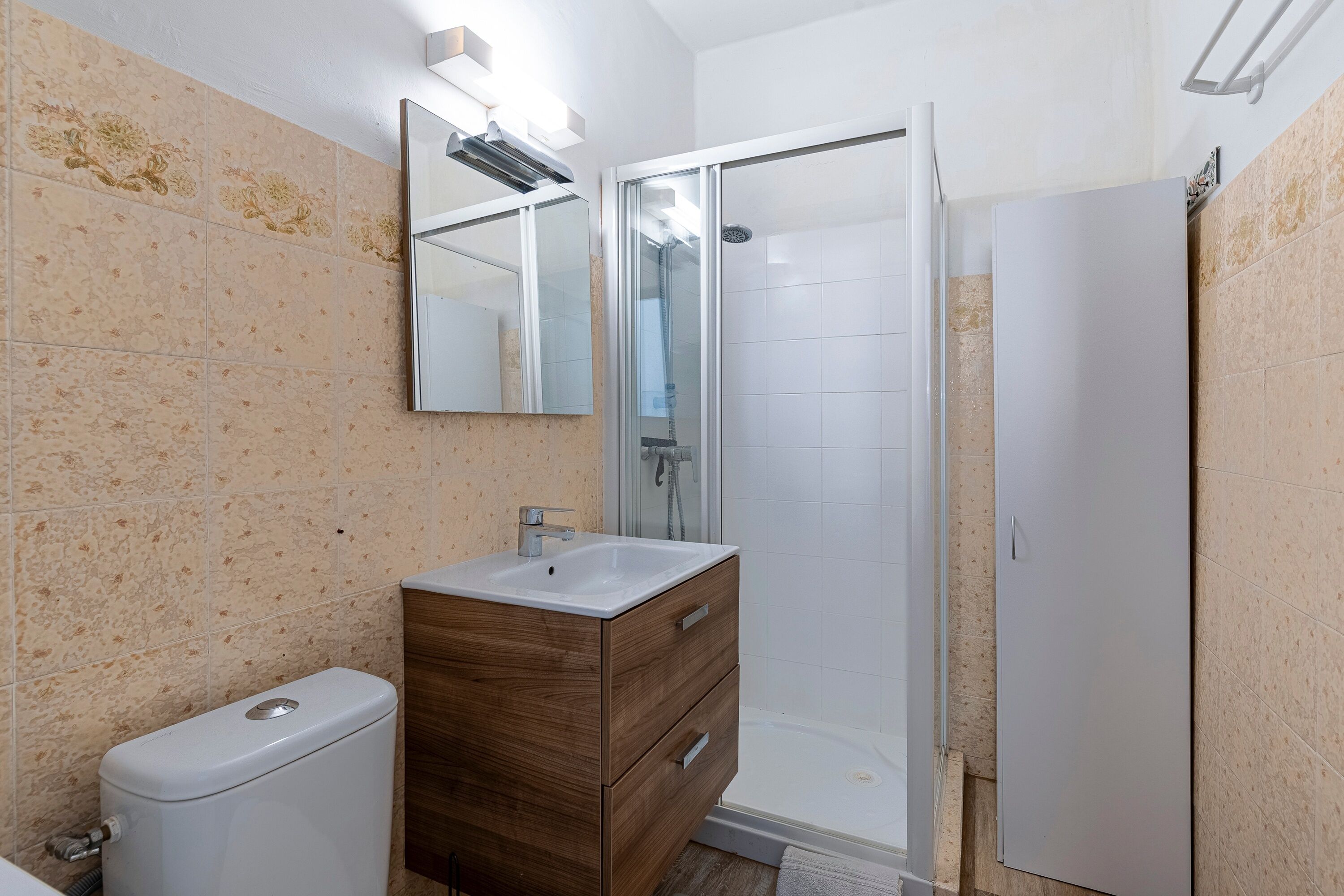 Un bagno con il water, un mobiletto contenitore in legno con lavabo, uno specchio e una cabina doccia in vetro.