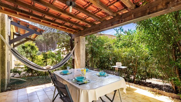 An outdoor patio with a table set for dining, surrounded by greenery and a hammock. - Maison Agosta Plage - Pour 5 à 500 m de la plage (Albitreccia)