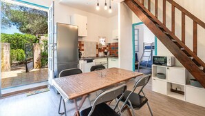 A modern kitchen with a dining area, wooden staircase, and a view of the outdoors. - Maison Agosta Plage - Pour 5 à 500 m de la plage (Albitreccia)