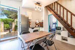 A modern kitchen with a dining area, wooden staircase, and a view of the outdoors. - Maison Agosta Plage - Pour 5 à 500 m de la plage (Albitreccia)