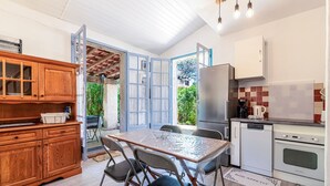 A compact kitchen with a dining table, chairs, wooden cabinets, a refrigerator, an oven, and a view of the outdoors. - Maison Agosta Plage - Pour 5 à 500 m de la plage (Albitreccia)