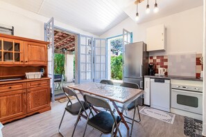 A compact kitchen with a dining table, chairs, wooden cabinets, a refrigerator, an oven, and a view of the outdoors. - Maison Agosta Plage - Pour 5 à 500 m de la plage (Albitreccia)