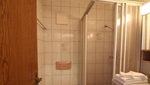 Et badeværelse med toilet, bruser og en stabel håndklæder.