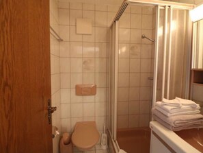 Ein Badezimmer mit Toilette, Dusche und einem Stapel Handtücher.
